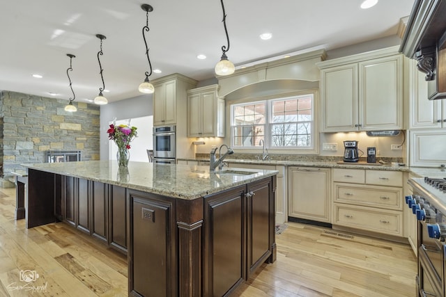 kitchen with a kitchen island with sink, cream cabinetry, a sink, and range