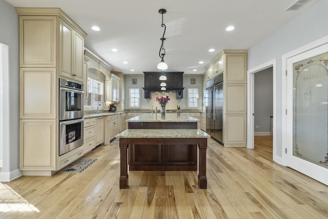 kitchen with visible vents, cream cabinets, appliances with stainless steel finishes, light wood-style floors, and a kitchen island