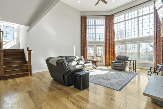 living room with a high ceiling, a ceiling fan, baseboards, stairs, and light wood finished floors