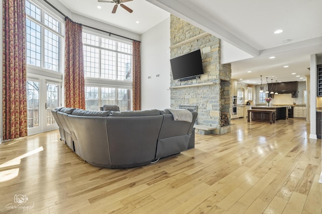 living room featuring ceiling fan, recessed lighting, a fireplace, a towering ceiling, and light wood finished floors