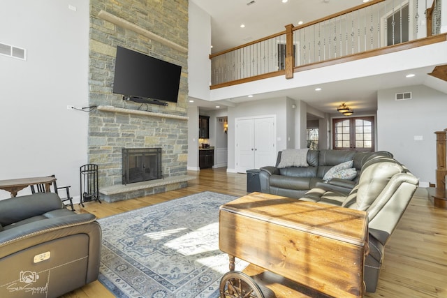 living area with a stone fireplace, a high ceiling, wood finished floors, and visible vents