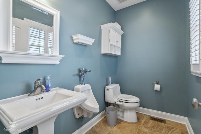 half bath featuring toilet, a sink, visible vents, baseboards, and tile patterned floors