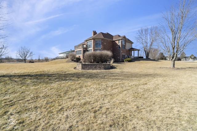 view of side of property with a chimney, a lawn, and brick siding