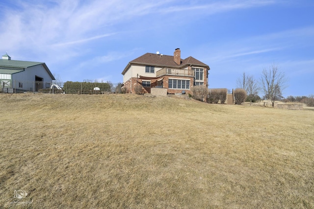 back of house featuring a chimney, an outbuilding, fence, a yard, and brick siding