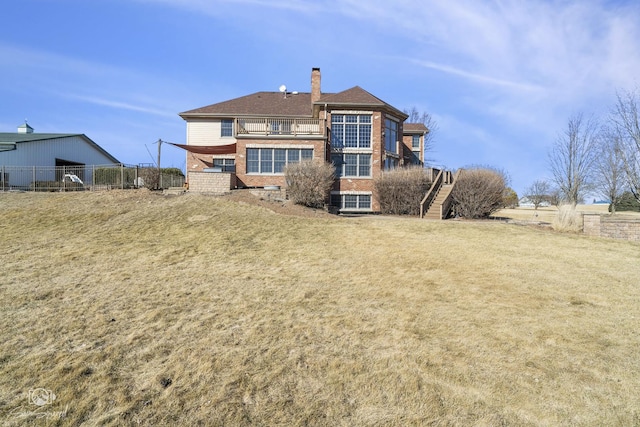 back of house featuring brick siding, fence, stairs, a yard, and a chimney