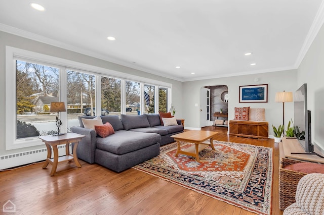 living room featuring baseboard heating, ornamental molding, hardwood / wood-style floors, and a healthy amount of sunlight