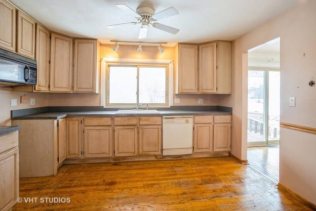 kitchen with light wood finished floors, dark countertops, a sink, black microwave, and dishwasher