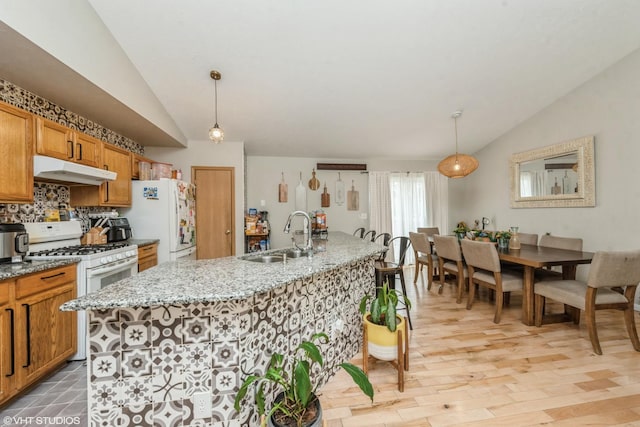 kitchen featuring a kitchen island with sink, sink, decorative light fixtures, and white appliances