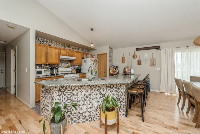 kitchen with lofted ceiling, sink, hanging light fixtures, white appliances, and light hardwood / wood-style floors