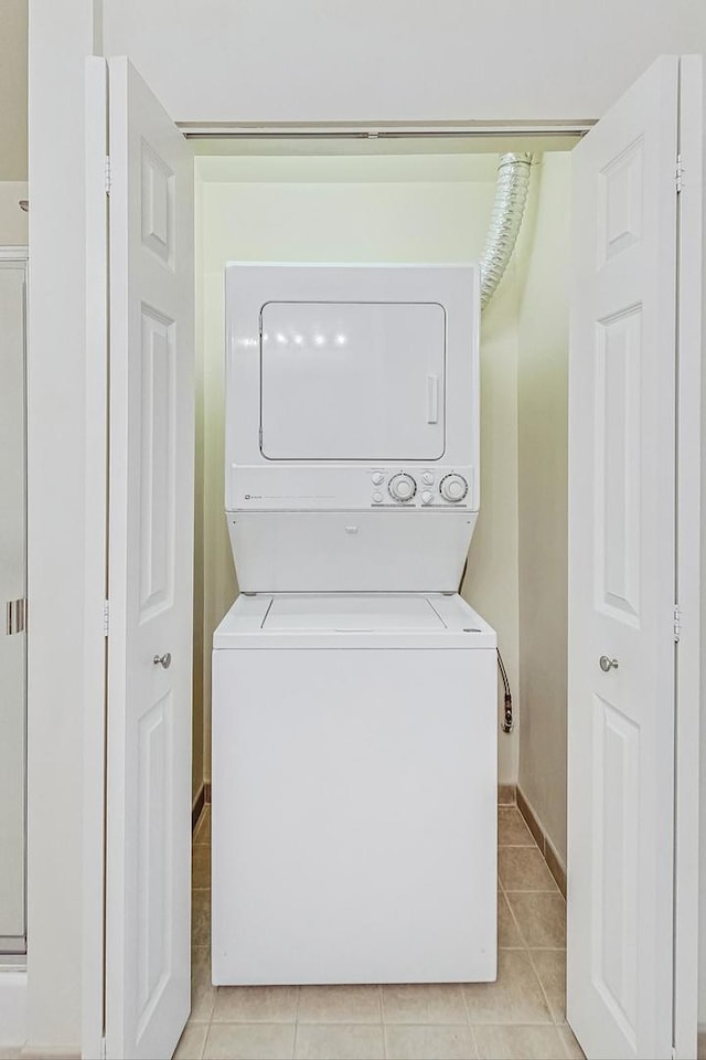 laundry room featuring stacked washer / drying machine and light tile patterned flooring