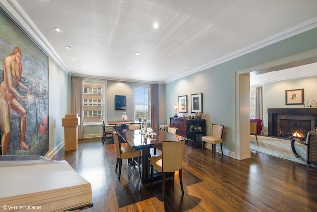 dining room featuring baseboards, ornamental molding, dark wood-style flooring, a lit fireplace, and recessed lighting