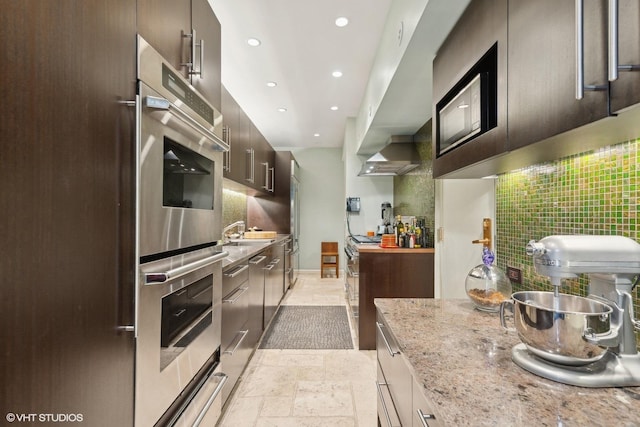 kitchen with double oven, dark brown cabinetry, a warming drawer, tasteful backsplash, and stone tile flooring