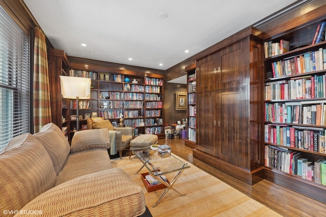 sitting room with wall of books, wood finished floors, and recessed lighting