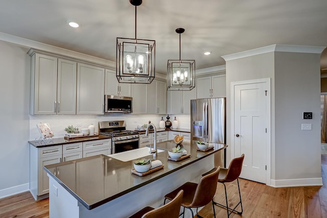 kitchen featuring pendant lighting, sink, stainless steel appliances, a center island with sink, and light hardwood / wood-style flooring