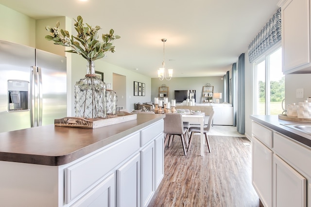 kitchen with stainless steel fridge, white cabinets, a chandelier, hanging light fixtures, and light hardwood / wood-style flooring