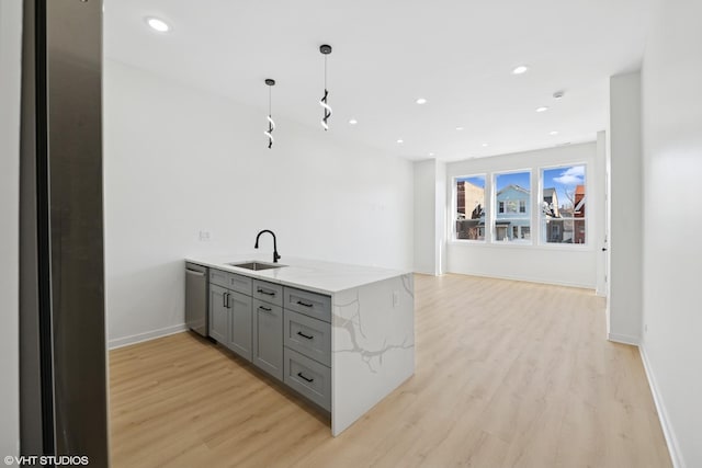 kitchen with light wood-style flooring, light stone countertops, gray cabinets, stainless steel dishwasher, and a sink