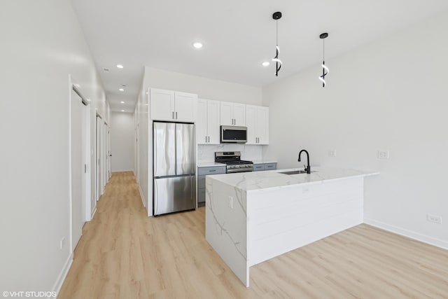 kitchen with a peninsula, appliances with stainless steel finishes, a sink, and light wood-style flooring