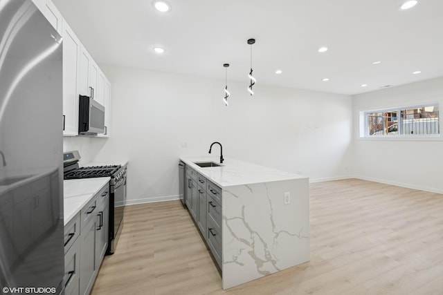 kitchen with a peninsula, gray cabinets, stainless steel appliances, light wood-type flooring, and a sink