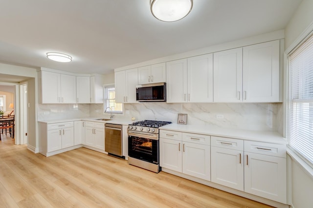 kitchen with appliances with stainless steel finishes, light hardwood / wood-style floors, sink, and white cabinets