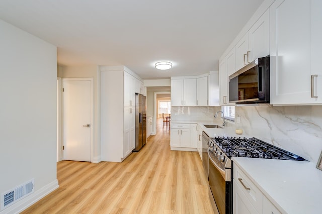 kitchen with sink, stainless steel appliances, tasteful backsplash, light hardwood / wood-style floors, and white cabinets