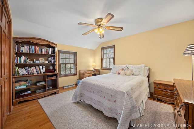 bedroom with baseboards, visible vents, light wood-style flooring, ceiling fan, and vaulted ceiling