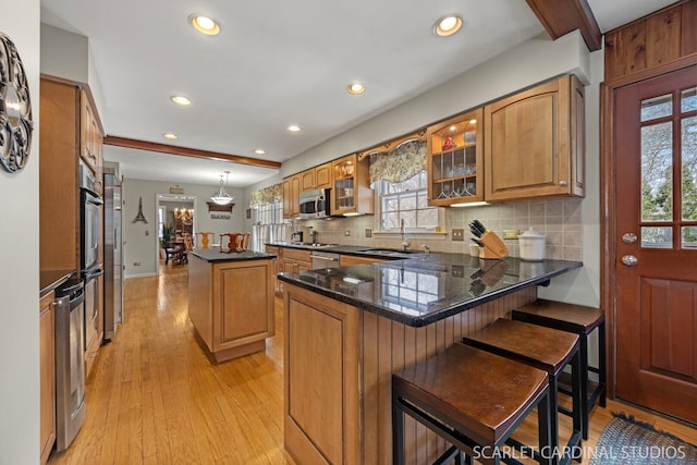 kitchen featuring brown cabinets, a sink, a peninsula, appliances with stainless steel finishes, and light wood finished floors