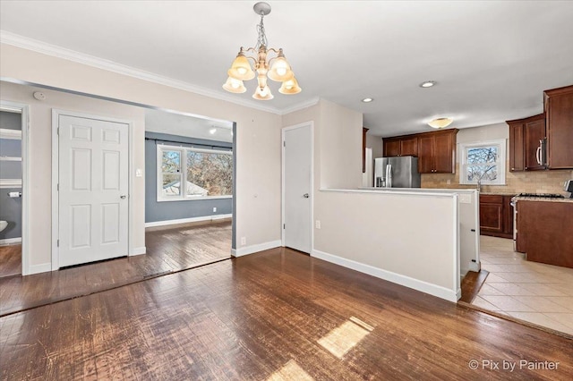 kitchen featuring baseboards, wood finished floors, decorative light fixtures, stainless steel appliances, and light countertops