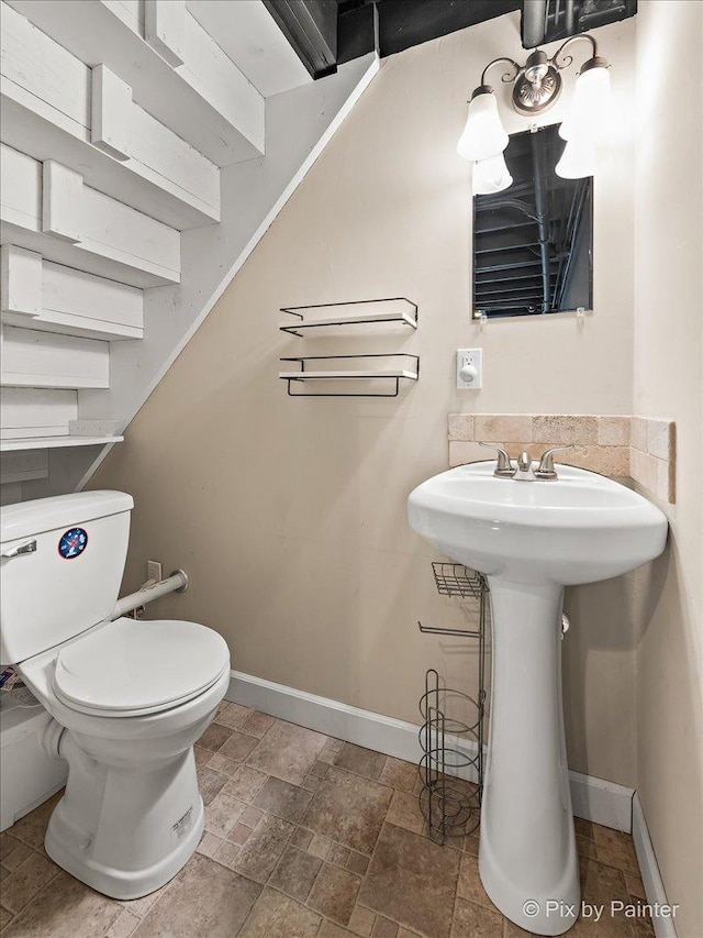 half bathroom with toilet, stone finish floor, baseboards, and a sink