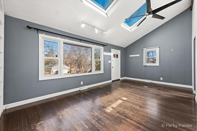 empty room featuring hardwood / wood-style flooring, vaulted ceiling with skylight, baseboards, and a ceiling fan