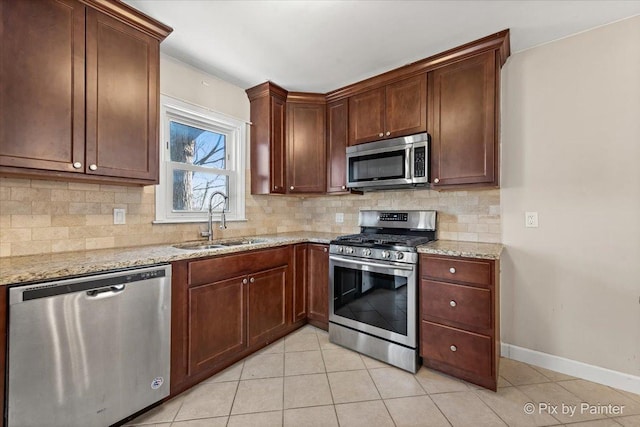 kitchen with appliances with stainless steel finishes, light stone countertops, a sink, and tasteful backsplash