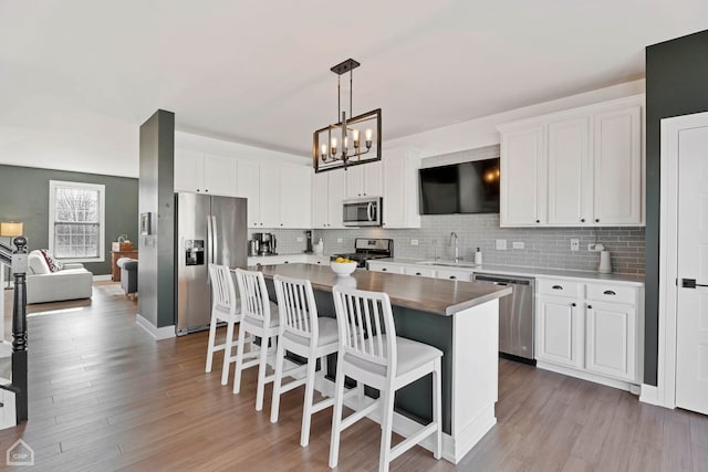 kitchen featuring a kitchen island, appliances with stainless steel finishes, decorative light fixtures, a breakfast bar area, and white cabinets