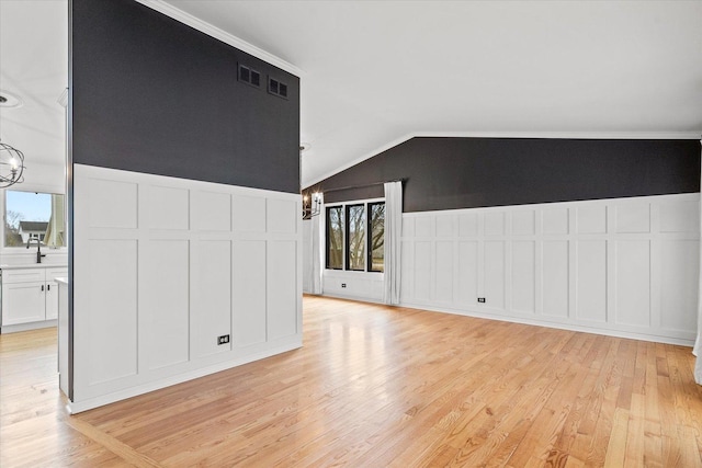 unfurnished living room with lofted ceiling, a decorative wall, light wood-type flooring, and a notable chandelier