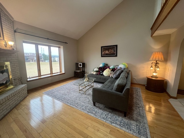 living room with high vaulted ceiling, a brick fireplace, and light wood-type flooring