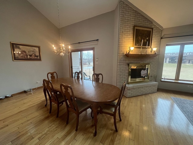 dining room with high vaulted ceiling, light hardwood / wood-style floors, a brick fireplace, and a notable chandelier