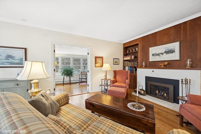 living room with a fireplace, built in features, baseboard heating, and light hardwood / wood-style floors