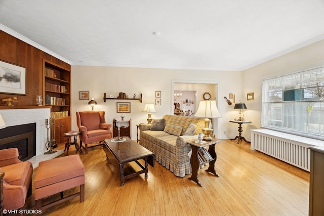 living room featuring radiator heating unit, built in features, light hardwood / wood-style floors, crown molding, and a brick fireplace