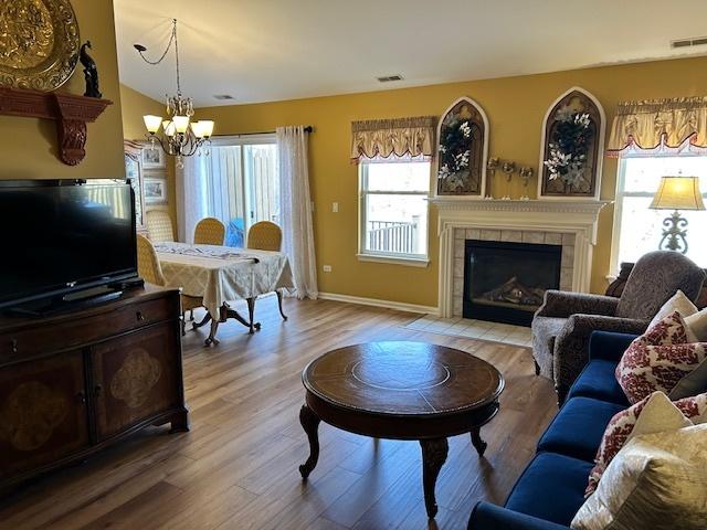 living room featuring a tile fireplace, wood-type flooring, vaulted ceiling, and an inviting chandelier