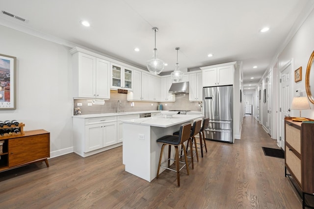 kitchen featuring white cabinetry, wall chimney range hood, decorative light fixtures, and stainless steel appliances