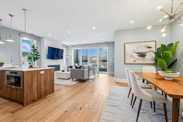 kitchen featuring pendant lighting, sink, oven, a kitchen island with sink, and light hardwood / wood-style floors