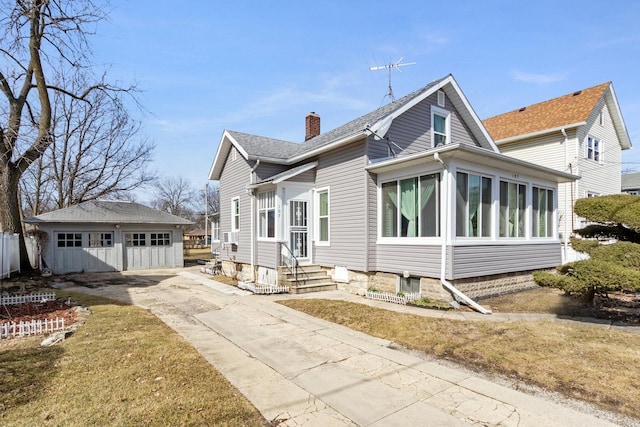 view of front of property featuring a shingled roof, a detached garage, entry steps, a chimney, and an outbuilding