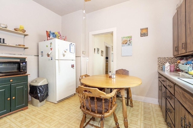 kitchen featuring black microwave, light floors, light countertops, freestanding refrigerator, and open shelves