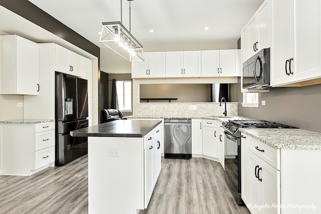 kitchen featuring pendant lighting, white cabinetry, a center island, black appliances, and light hardwood / wood-style flooring