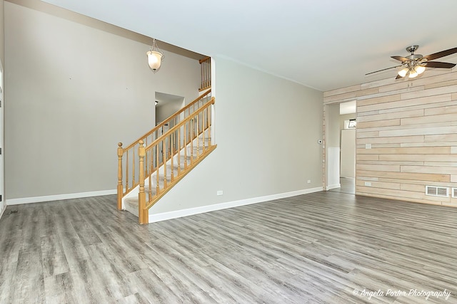 unfurnished living room with ceiling fan, wooden walls, and light hardwood / wood-style flooring