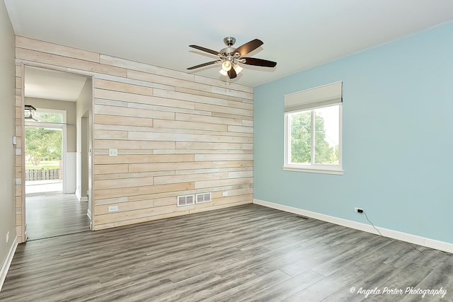 spare room with hardwood / wood-style flooring, ceiling fan, and wood walls