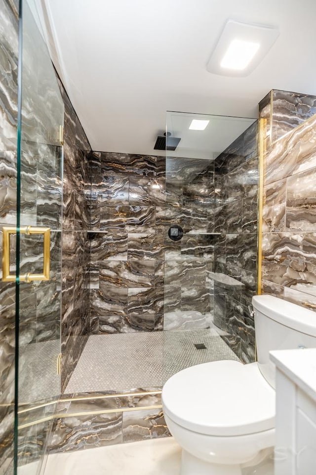 bathroom with vanity, a shower with shower door, tile walls, and toilet