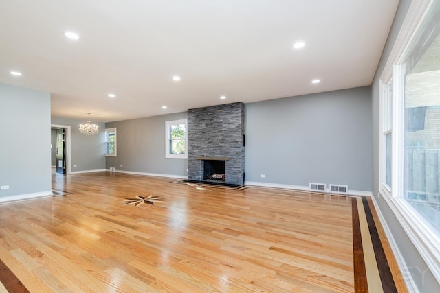 unfurnished living room featuring a stone fireplace, light hardwood / wood-style flooring, and a chandelier