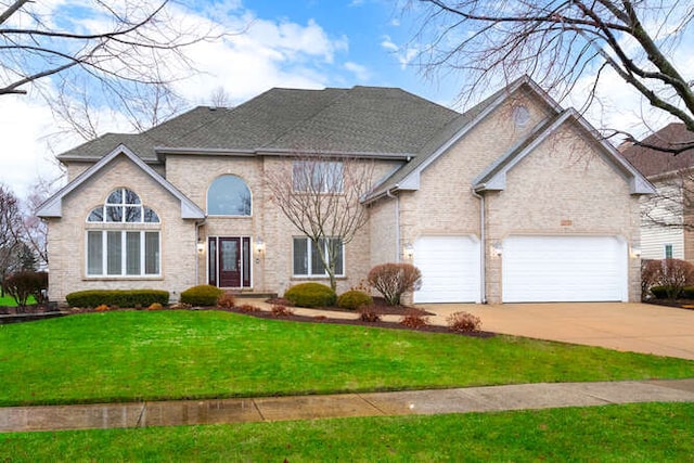 traditional-style home with driveway, an attached garage, a shingled roof, and a front yard