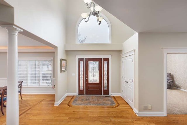 foyer featuring a chandelier, a towering ceiling, light wood-style flooring, and ornate columns