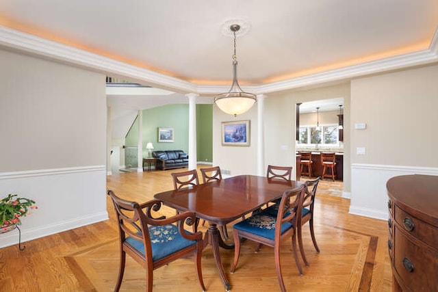 dining area with a tray ceiling, baseboards, light wood finished floors, and ornate columns