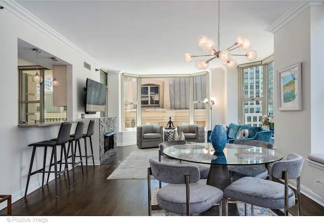 dining room with crown molding, dark hardwood / wood-style flooring, an inviting chandelier, and a stone fireplace